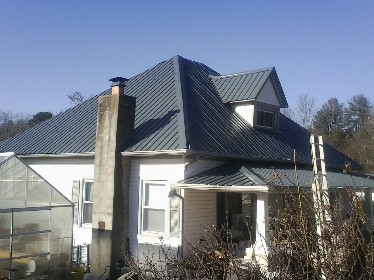 Dark blue standing seam metal roof on a white farmhouse with dormer — Slate & Tile Roof Repair by Roofing Brothers in Cottage Grove