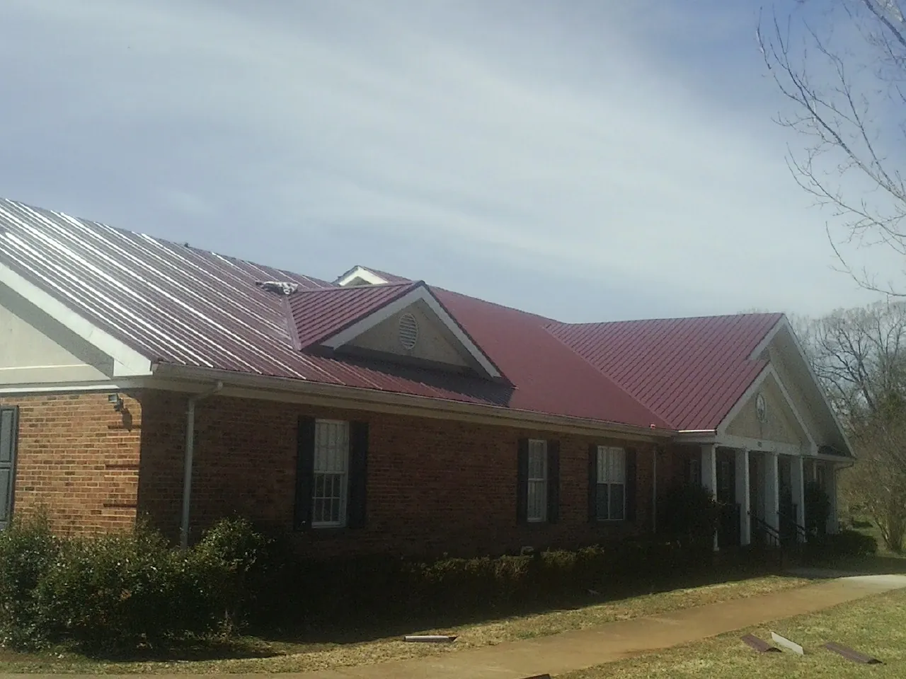 Red metal roof with gabled entries on a long brick building, from a Hail Damage Roof Repair job in Cottage Grove