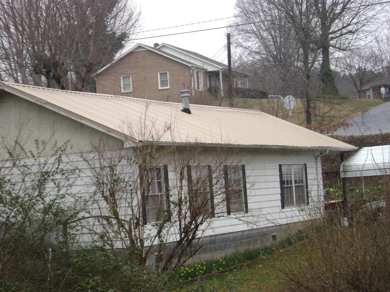 Tan metal roof on a white sided house set into a hillside — Commercial Roofing by Roofing Brothers in Cottage Grove