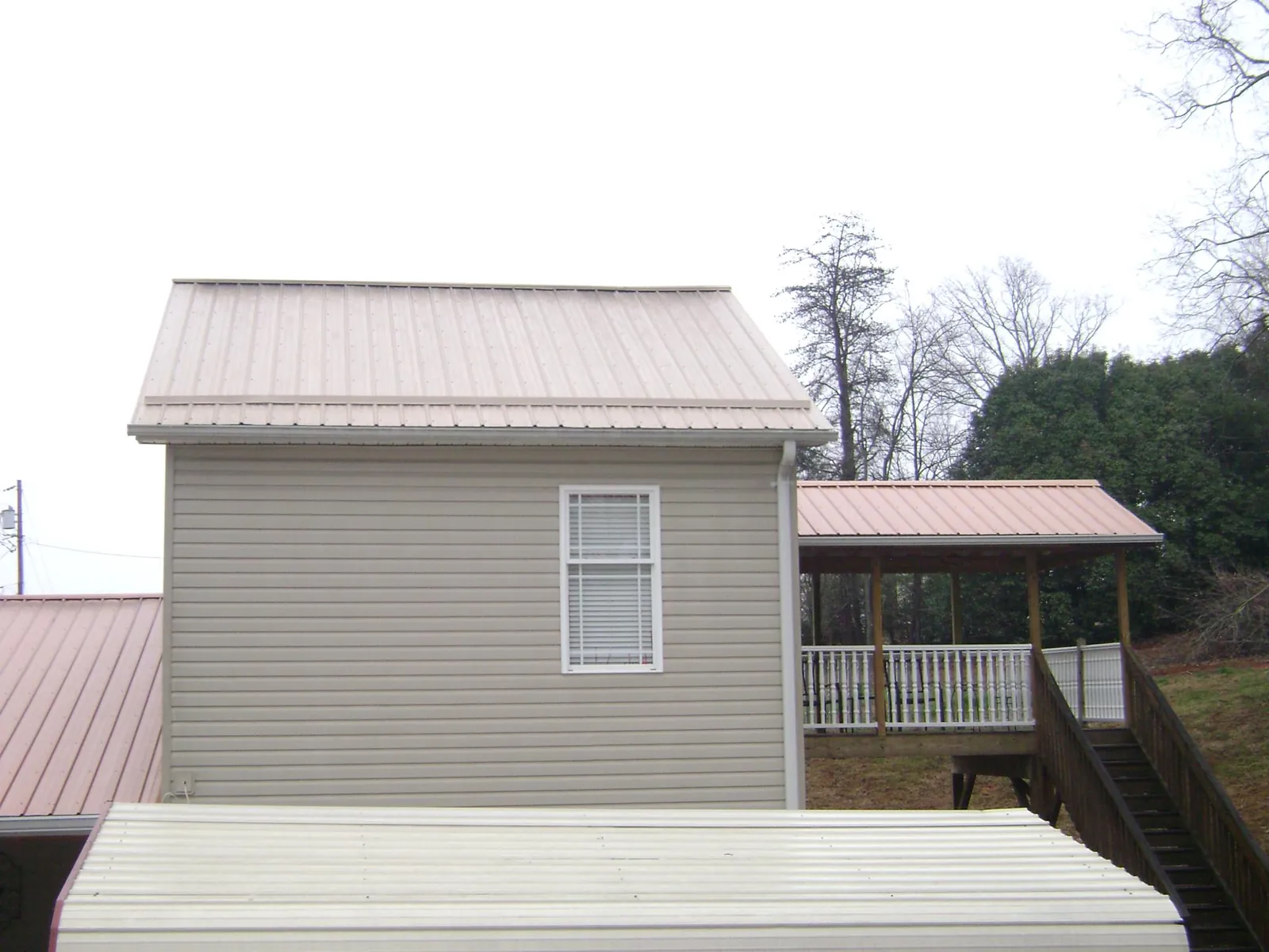 Tan metal roofs on a two story addition and attached porch, from a Roof Replacement job in Cottage Grove
