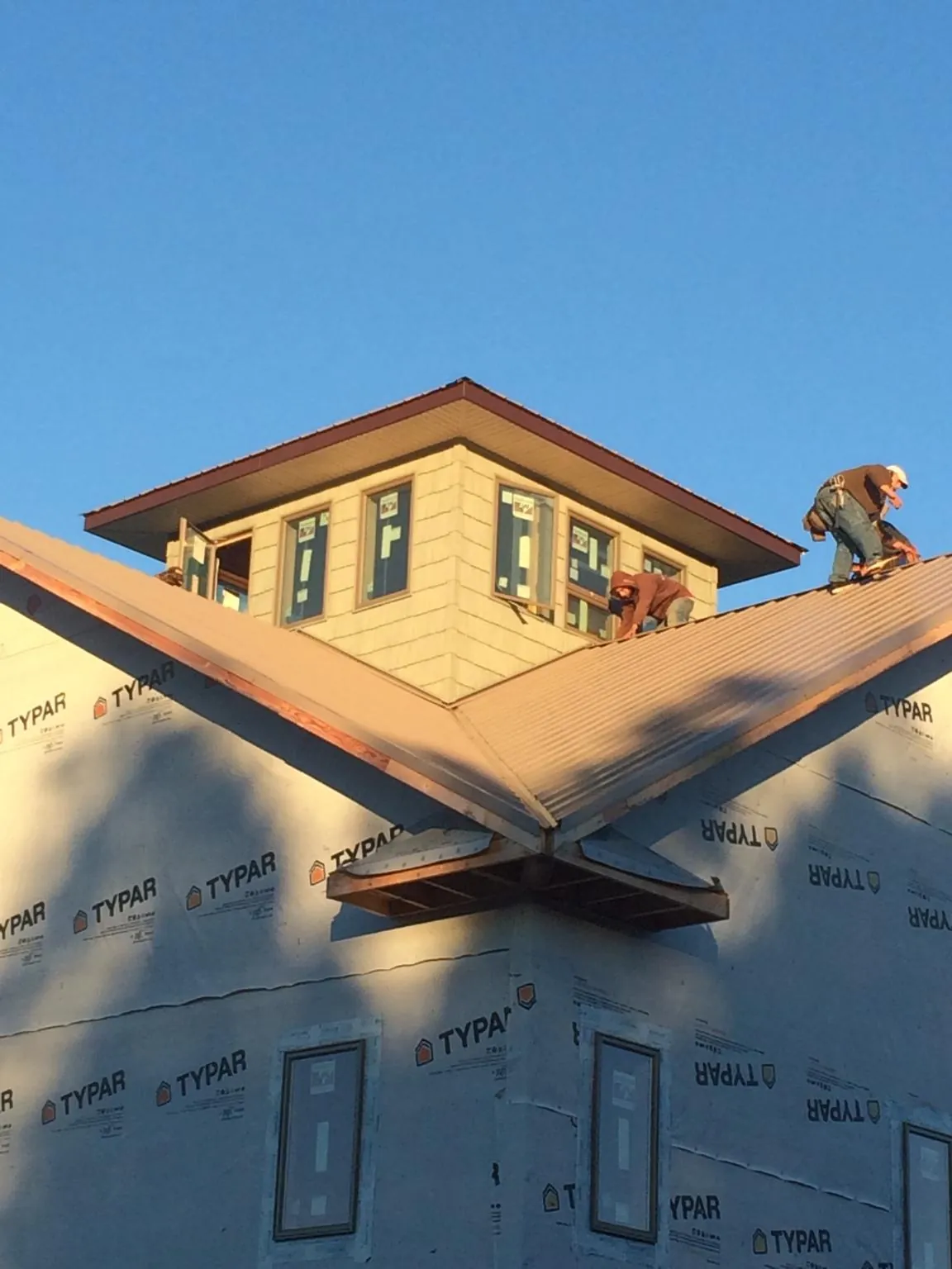 Roofers working around a rooftop cupola on a new metal roof at sunset — Roof Waterproofing in Cottage Grove by Roofing Brothers